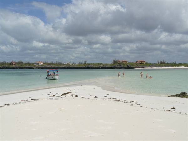 White boat moored in turquoise water, tourists wading on the shallow sandbank