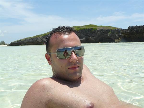 Man in mirrored sunglasses in turquoise water, green rocky cliffs behind