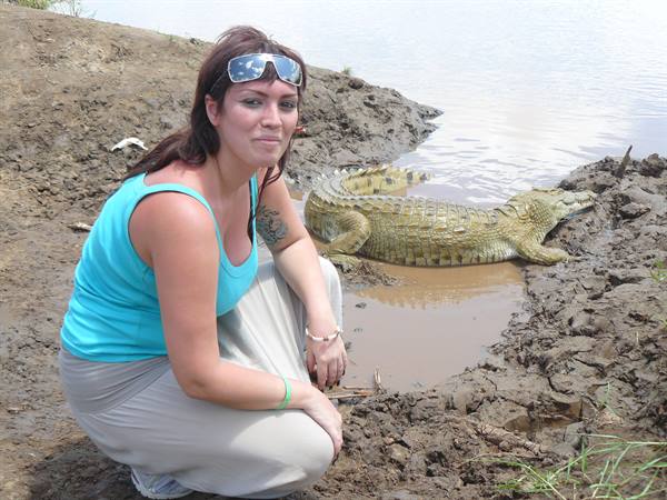 Woman crouching beside a crocodile on mud near the water