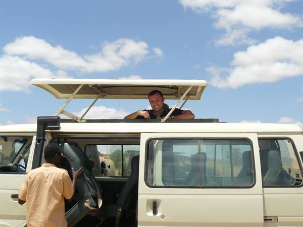 Tourist leaning out of open safari van rooftop, driver nearby