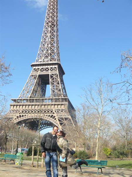 Couple kissing beneath the iron Eiffel Tower, winter park with green benches