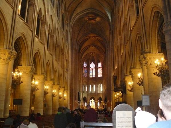 Inside Notre-Dame Cathedral: gothic nave, lit chandeliers and worshippers among pews