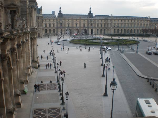 Tourists walking across the Louvre's cour Napoléon, among lampposts and circular garden