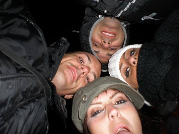 Four friends in winter jackets huddle heads together at night, camera flash