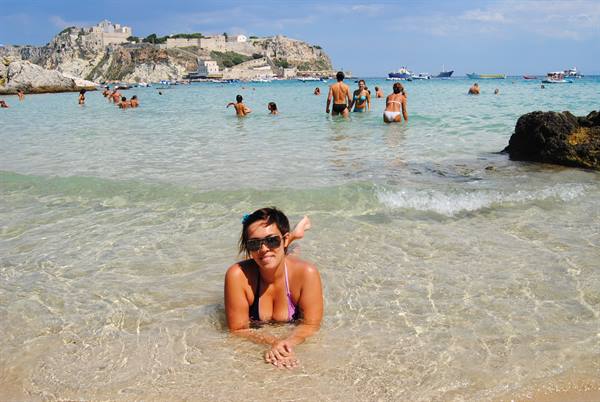 Girl in sunglasses lying in clear shallow water, swimmers and fortress island behind