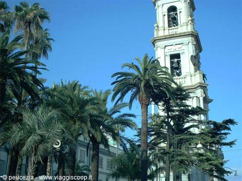 White bell tower of Pompei sanctuary among palm trees, blue sky
