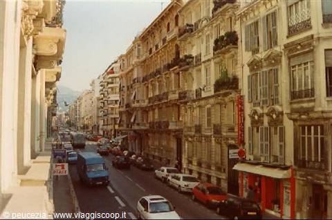 City street lined with Belle Époque buildings, parked cars and shop signs