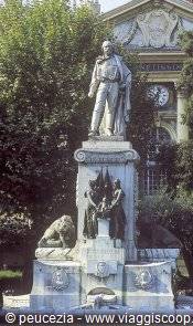 Stone statue of standing man on pedestal with carved lions, trees behind