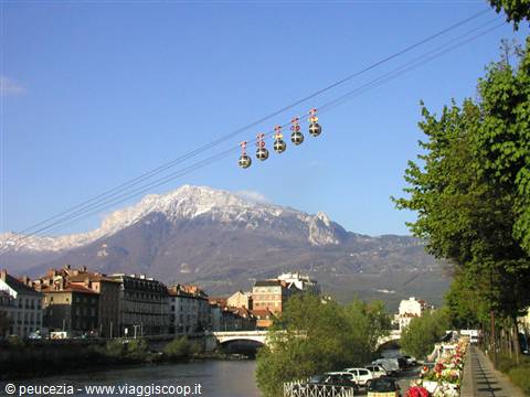 Cable cars suspended above the river in Grenoble, snowy mountain in the background