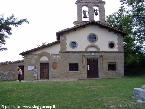 Tourists walk past a small stone church with a bell tower