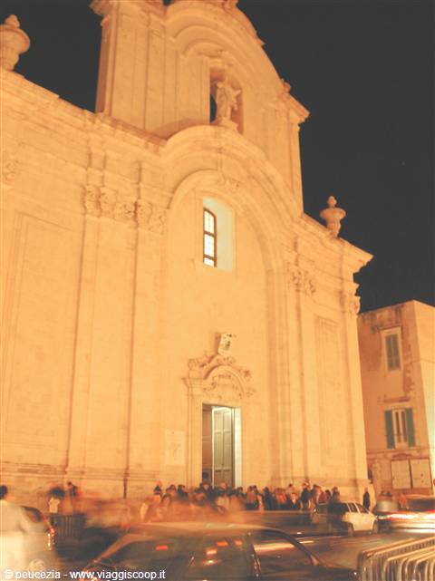 Baroque church facade in pale stone lit at night, crowd at entrance