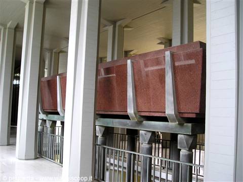 Red granite sarcophagi suspended on steel beams among white columns