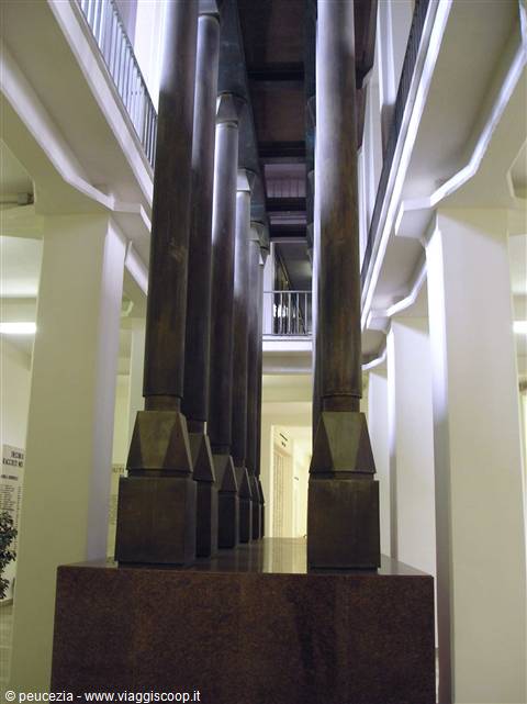 Bronze columns on a stone base inside a two-level white atrium