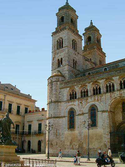 Altamura Cathedral, pale stone facade with towers, sunny square with passersby