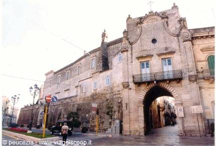 Porta Napoli in Lecce, limestone arch with wrought-iron balcony, daylight, pedestrians