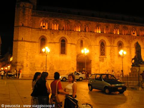 People chat at night in front of the illuminated stone church facade