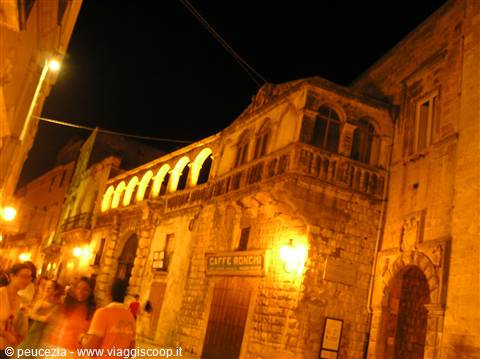 Stone palace with arched loggia lit at night, people strolling in the old town