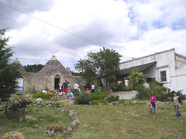 Visitors near stone trullo in Alberobello, grass and old cart