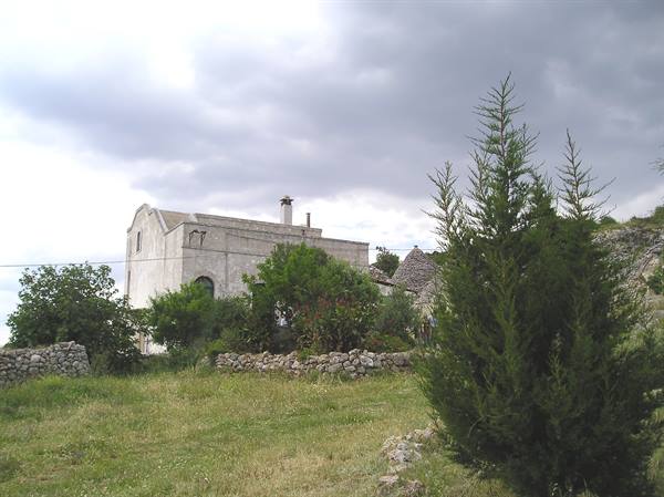 Stone trullo and farmhouse behind dry stone walls and cypress, cloudy sky