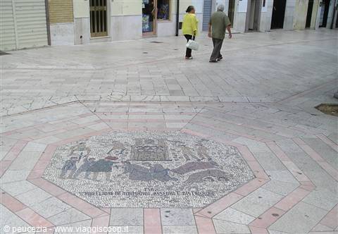 Marble square with Assisi's twin-city mosaic inlay, people walking past shops