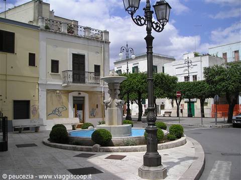 Round stone fountain with blue basin, wrought iron lampposts and whitewashed buildings