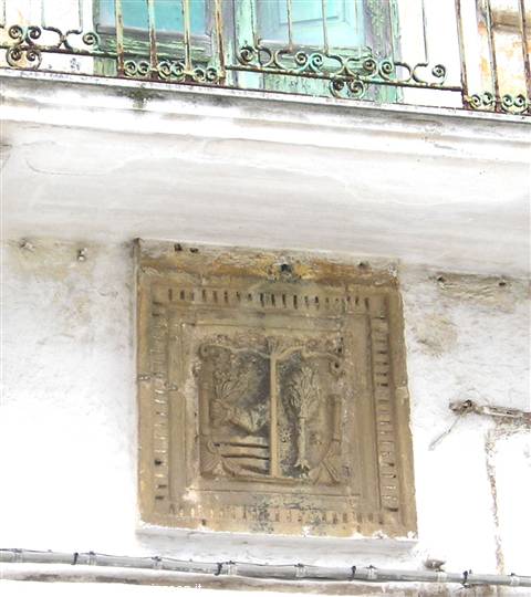 Carved stone coat of arms on white facade beneath a wrought iron balcony