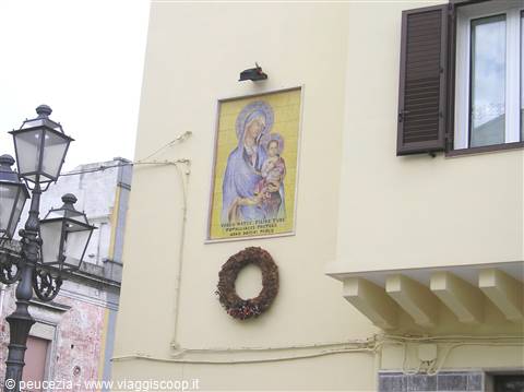 Fresco of Madonna and Child on yellow wall, wreath below, wrought-iron street lamps