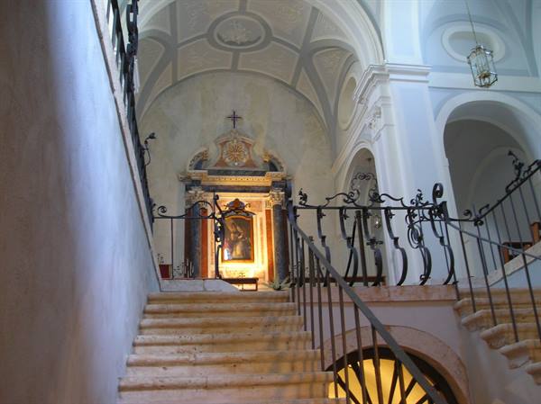 Stone staircase with wrought iron railing leads to an illuminated chapel