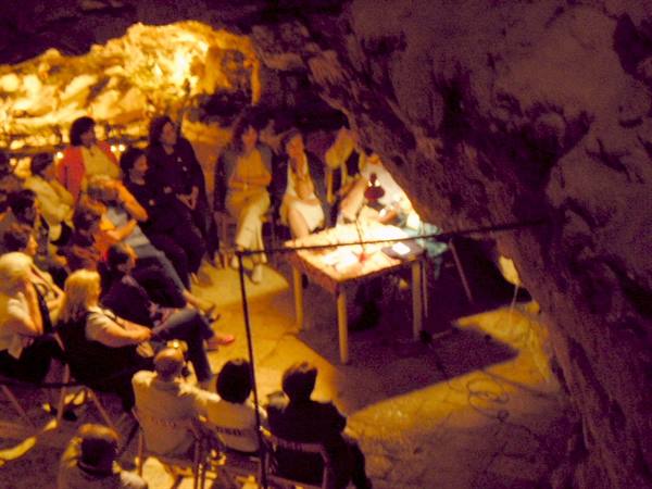 Visitors seated listening to a guide inside a yellow-lit cave