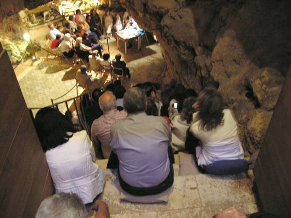 Visitors seated on stone steps inside a lit cave, resembling an auditorium