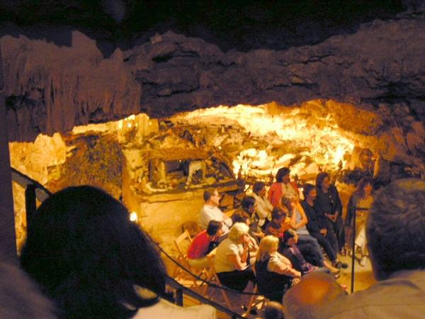 Visitors seated on chairs inside a cave lit by warm golden light