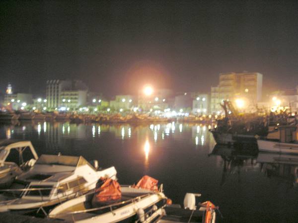 Boats moored at night in the harbor, city lights reflected on the water