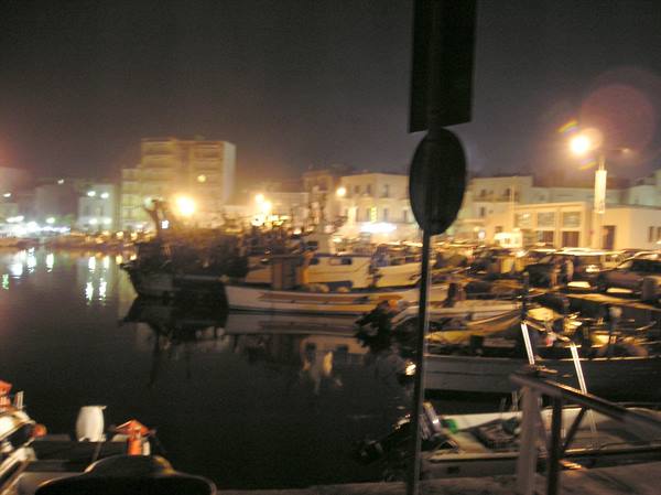 Fishing boats moored in the harbor at night, streetlights and buildings glowing on the water