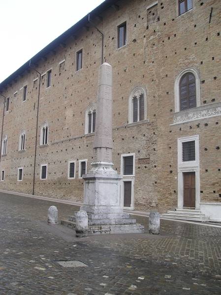 Marble obelisk on cobbled square in front of Urbino's Ducal Palace