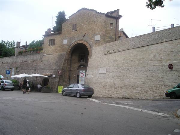 Old brick gate with arch, parked cars and people under umbrellas