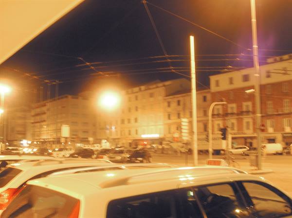 Cars up front under tram wires, streetlights glowing among nighttime buildings