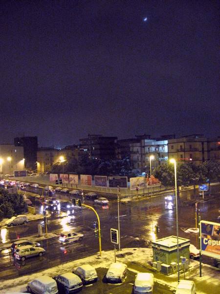 Snow-covered cars at a city intersection at night, streetlights glowing