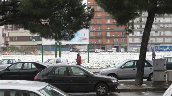 Cars parked along a snowy street, residential buildings in the background