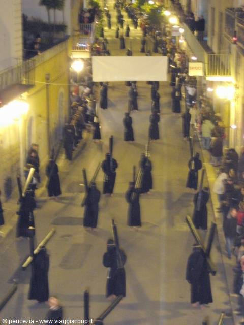 Black-hooded figures with wooden crosses marching in a night procession