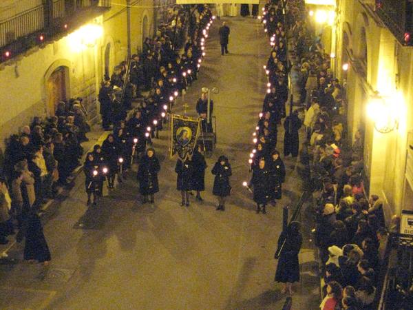 Night candle procession down the street, mourners in black, crowd watching