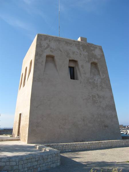 Plastered stone coastal tower under blue sky, low dry-stone walls in front