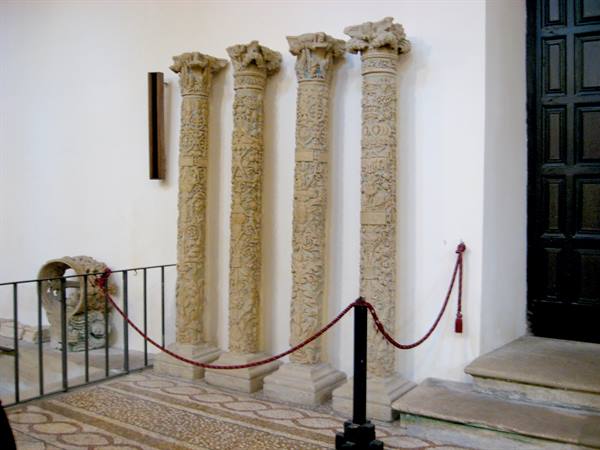 Four carved medieval stone columns against white wall, museum