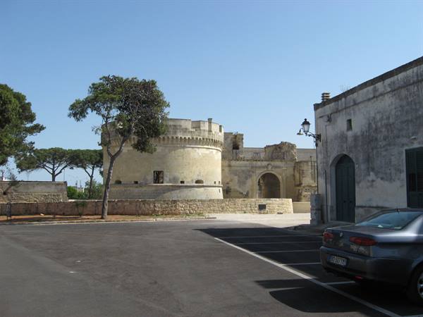 Round tower of Acaya castle beside a whitewashed building and parked car