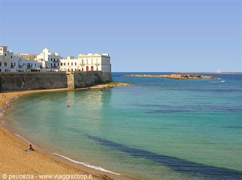 Sandy beach with white houses and old stone walls above turquoise water, Gallipoli