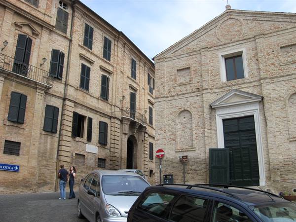 Brick palace and church with green shutters, parked cars and two people