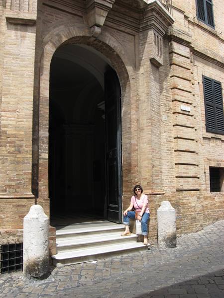 Woman sitting on steps of a brick arched doorway, cobblestone street