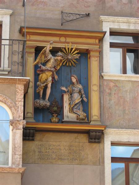 Niche with golden wooden Annunciation statues on a frescoed building facade
