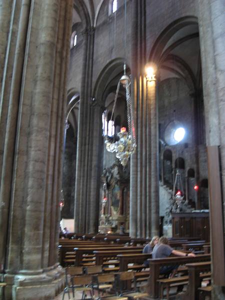 Cathedral interior with massive stone columns, silver chandelier and worshippers praying