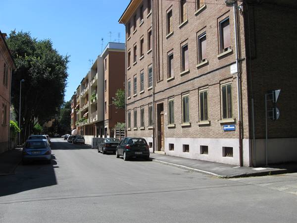 Cars parked along a residential street with brick buildings under sunny sky