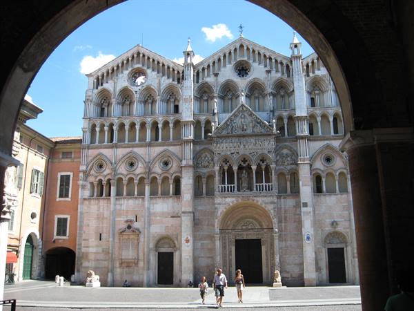 Ferrara Cathedral marble facade framed by an arch, tourists walking below